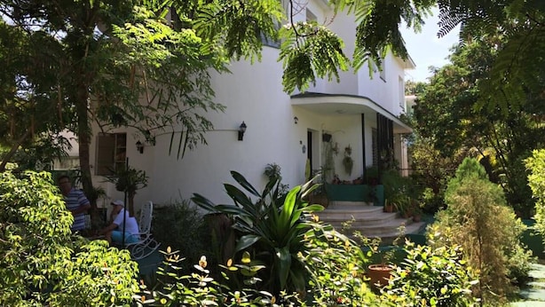A white building with a covered porch, surrounded by lush greenery and a small garden. - Casa Miramar Ileana Abella MIRAMAR (Havana)