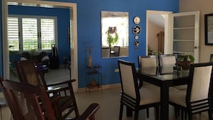 A dining area with a glass table and chairs, a blue wall, and a window with blinds. - Casa Miramar Ileana Abella MIRAMAR (Havana)