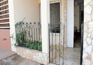 Entrada com piso de pedra, um portão de metal e um pequeno jardim.