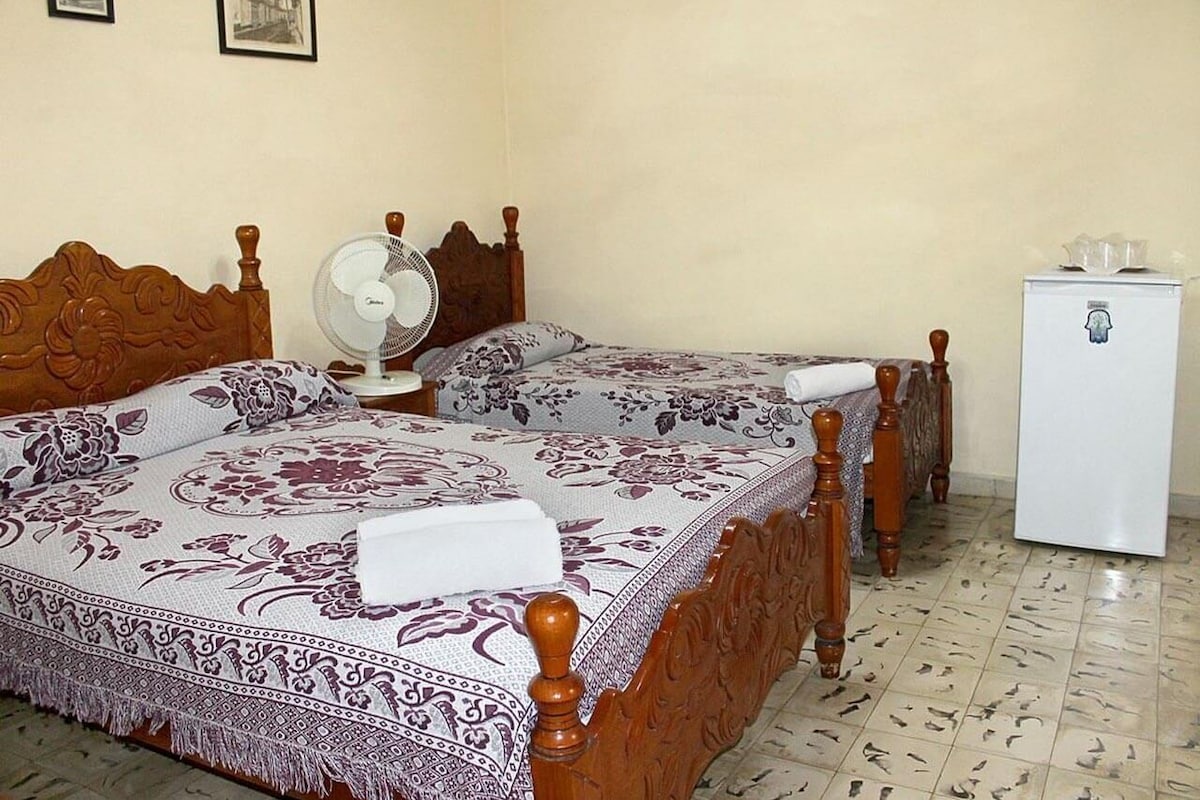 Ein Schlafzimmer mit zwei Holzbetten, einem Nachttisch mit Ventilator und einem kleinen Kühlschrank.
