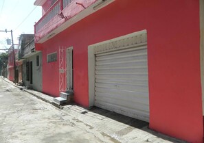 Un edificio rojo con una persiana metálica bajada, una reja y una acera de hormigón.