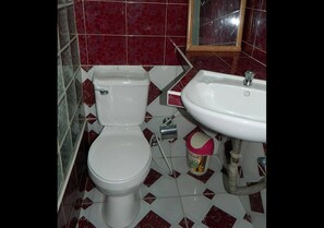 Un baño con inodoro y lavabo, suelo de baldosas y un espejo sobre el lavabo.