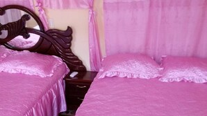 Een kamer met twee bedden, elk met een roze dekbedovertrek en passend kussen. Eén bed heeft een houten hoofdbord.