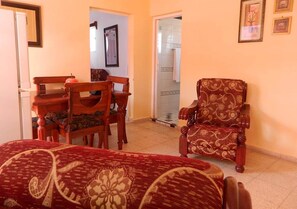 Una sala de estar con un sofá, una mesa de comedor de madera con sillas y un sillón estampado.