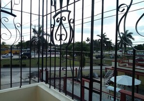 A balcony with a metal railing and a view of a street with cars and palm trees. - Hostal Betty SANTA MARTA (Cárdenas)