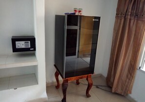 A room with a glass-fronted cabinet on a wooden stand, a small shelf with a device, and a window with curtains. - Hostal Betty SANTA MARTA (Cárdenas)