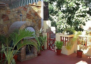 Surrounded by lush greenery, this charming courtyard features a stone-built outdoor oven and a rustic stone wall.