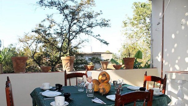 A dining table set outdoors with a green tablecloth, chairs, plates, cups, and a chef's hat. - Hostal El Corojo TRINIDAD (Trinidad)