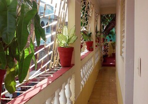 A corridor with potted plants on a balcony, a tiled floor, and a white railing. - Hostal El Corojo TRINIDAD (Trinidad)