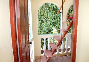 Eine Treppe mit roter Handlauf, die zu einem Balkon mit Blick auf grüne Pflanzen führt.