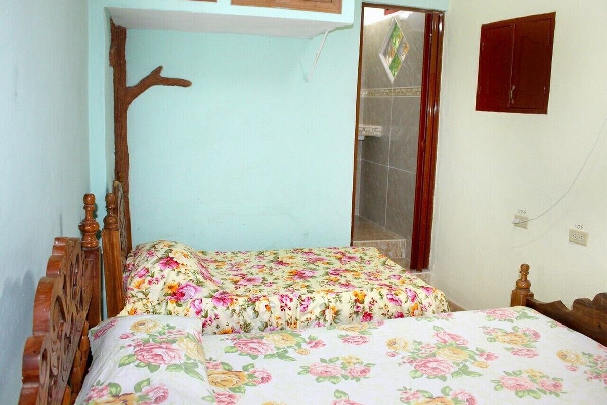 Ein Schlafzimmer mit zwei Holzbetten, floralem Bettzeug, einer Holz-Kopfteil und einem kleinen Fenster, sowie einem an der Wand befestigten Schrank.