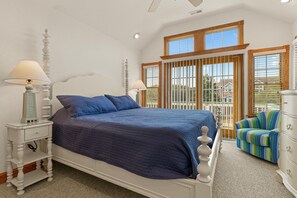 A bedroom with a large bed, two bedside tables, a dresser, and a view of the outside through large windows. - All Things Possible: Private Pool, Hot Tub, Close to Beach (Corolla)