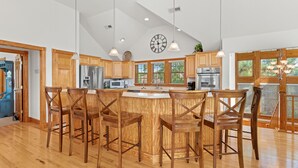 Une cuisine spacieuse avec des meubles en bois, un îlot central doté de tabourets et de grandes fenêtres.