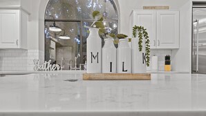 A kitchen with white cabinets, a marble countertop, and three white bottles with the letters "MIL" on them. - Stunning North Scottsdale Home w/Heated Pool and Hot Tub (Scottsdale)