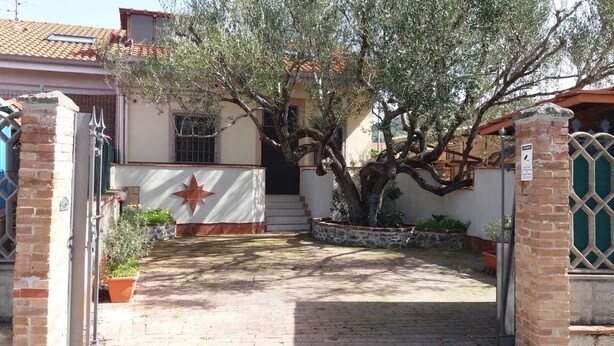 A courtyard with a tree, a gate, and a building with a star-shaped decoration. - Villa dei focesi (Marina di Ascea)