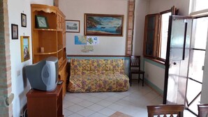 A living room with a sofa, a wooden cabinet, a television, and a painting on the wall. - Villa dei focesi (Marina di Ascea)