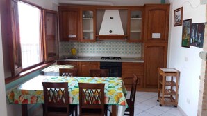 A kitchen with wooden cabinets, a gas stove, and a dining table with chairs. - Villa dei focesi (Marina di Ascea)