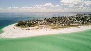 An aerial view of a coastal town with a beach, clear waters, and a dense cluster of houses.