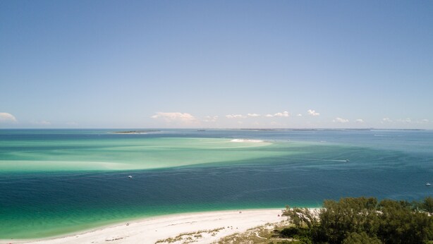 A coastal landscape with a beach, clear turquoise waters, and a distant ship. - West Bay Cove 131 · Skyway Views · 30-Night Min (Holmes Beach)