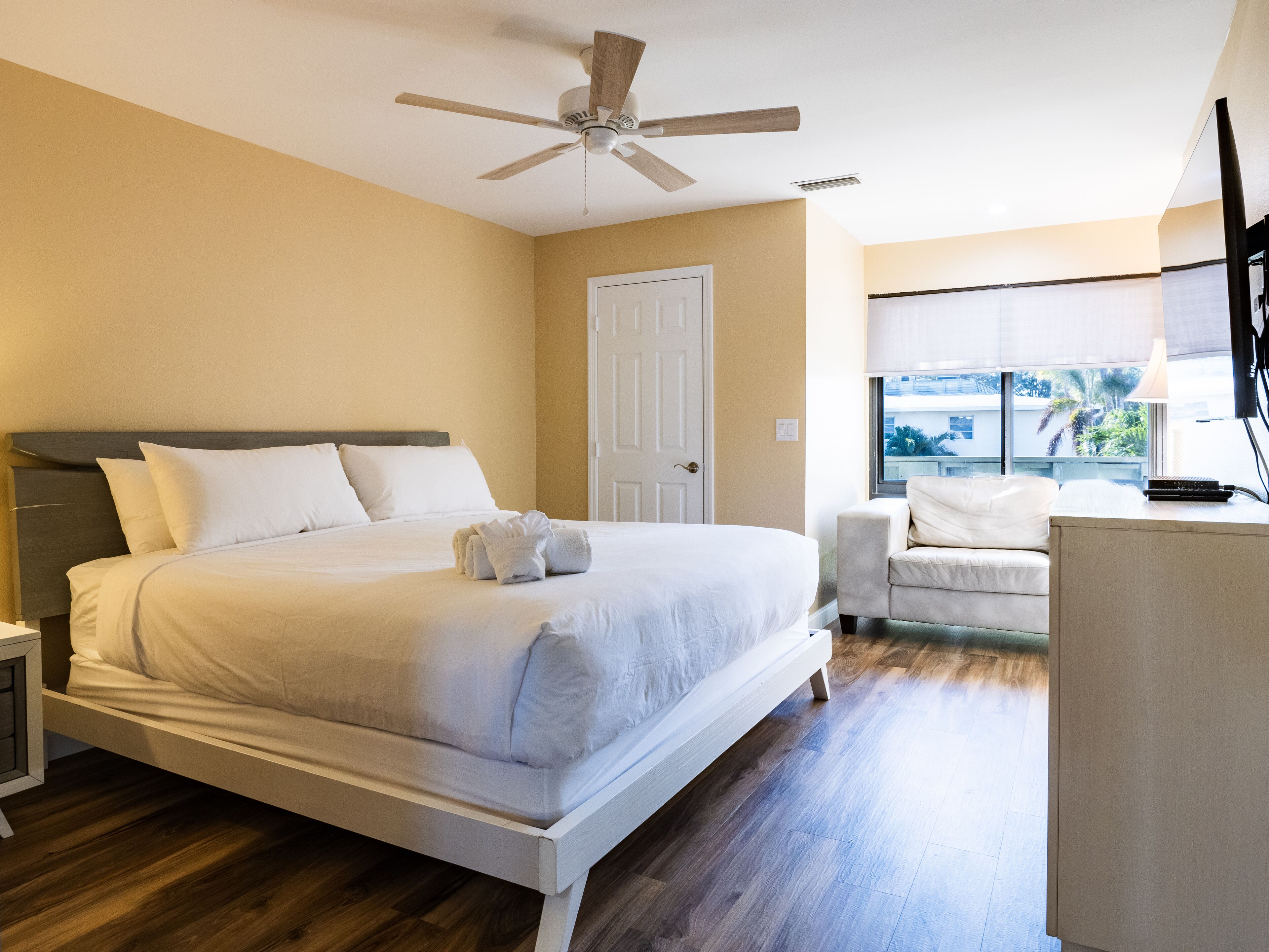 A neatly arranged bedroom with a bed, a chair, a desk, and a ceiling fan.