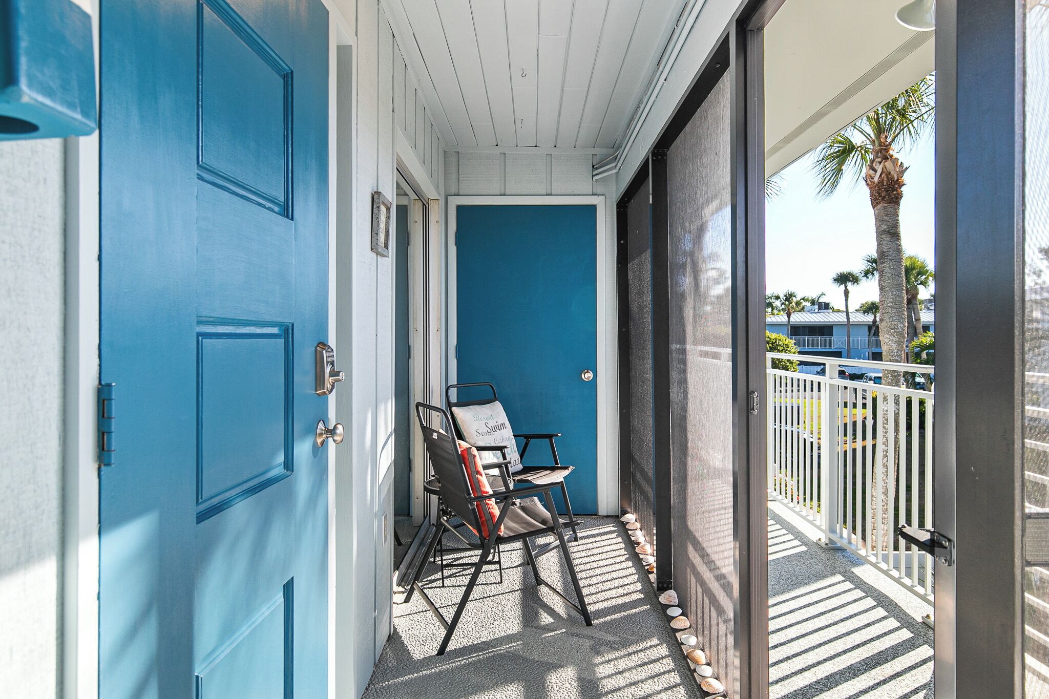A blue door with a chair and a white railing on a balcony.