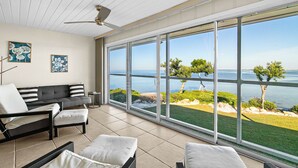 A modern living room with a large sliding glass door leading to a balcony with a view of the sea.