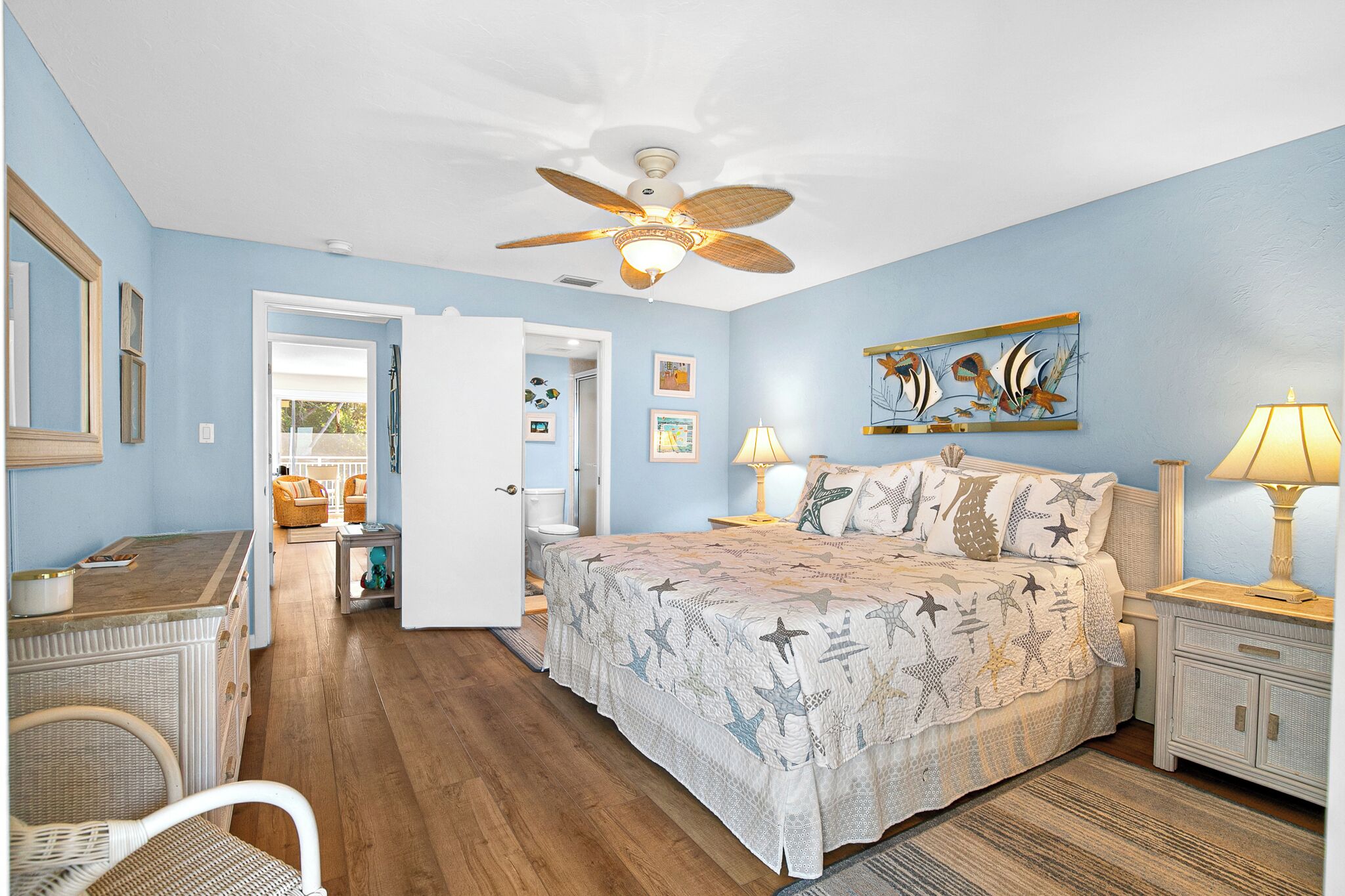 A bedroom with a bed, a ceiling fan, a nightstand, a lamp, and a door leading to another room.