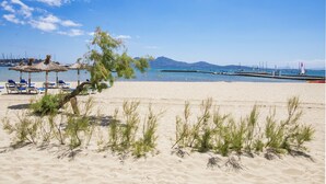 A beach with thatched umbrellas, lounge chairs, and a clear view of the sea and distant mountains.