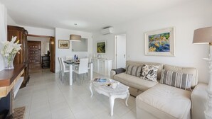 A modern living room with a beige sofa, a white coffee table, and a dining area with a white table and chairs.
