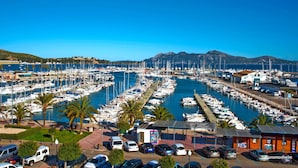 A marina with numerous boats docked, a parking area with cars, and a building with a sign.