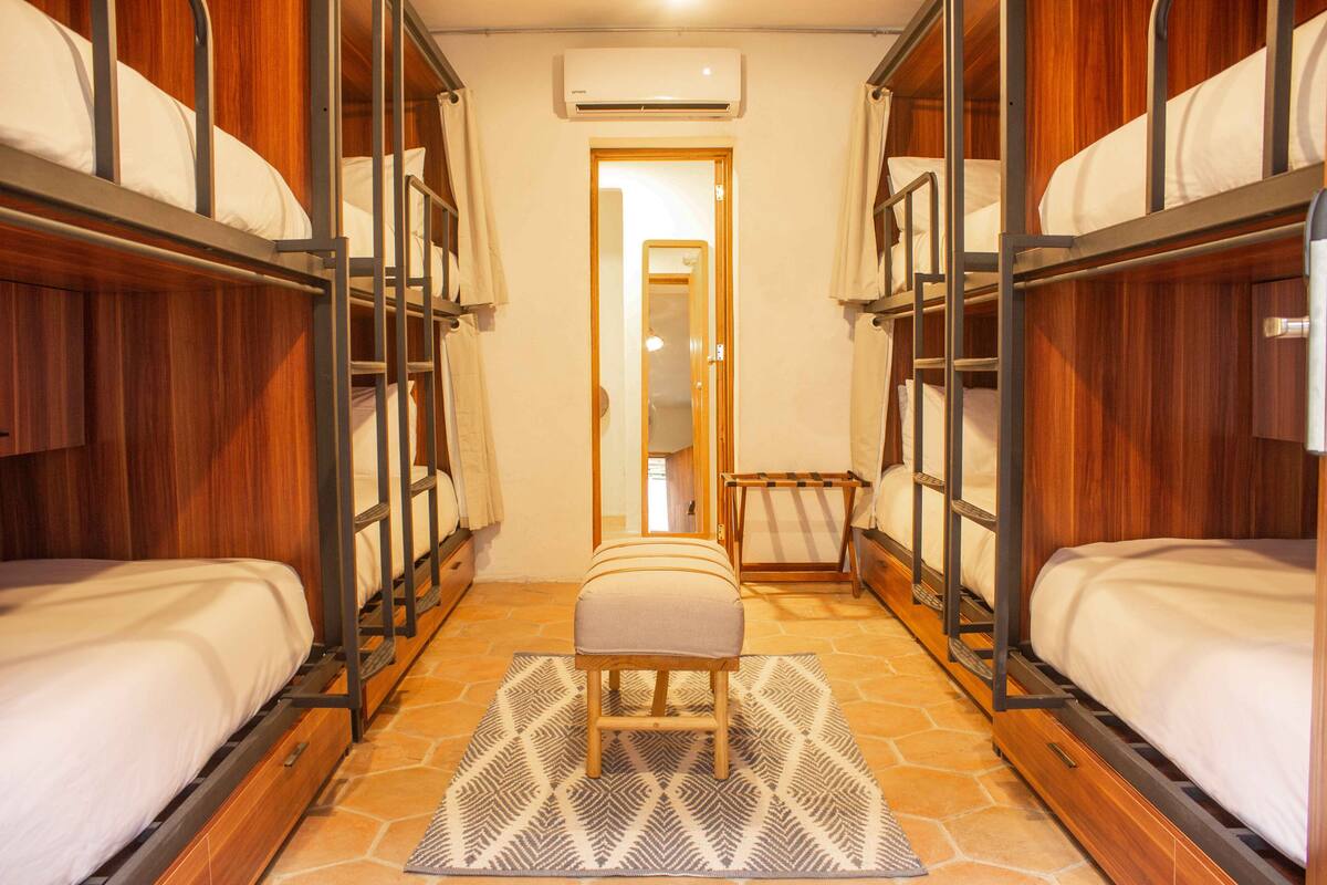 Ein Hotelzimmer mit Stockbetten, einer Sitzbank in der Mitte und einem gemusterten Teppich.