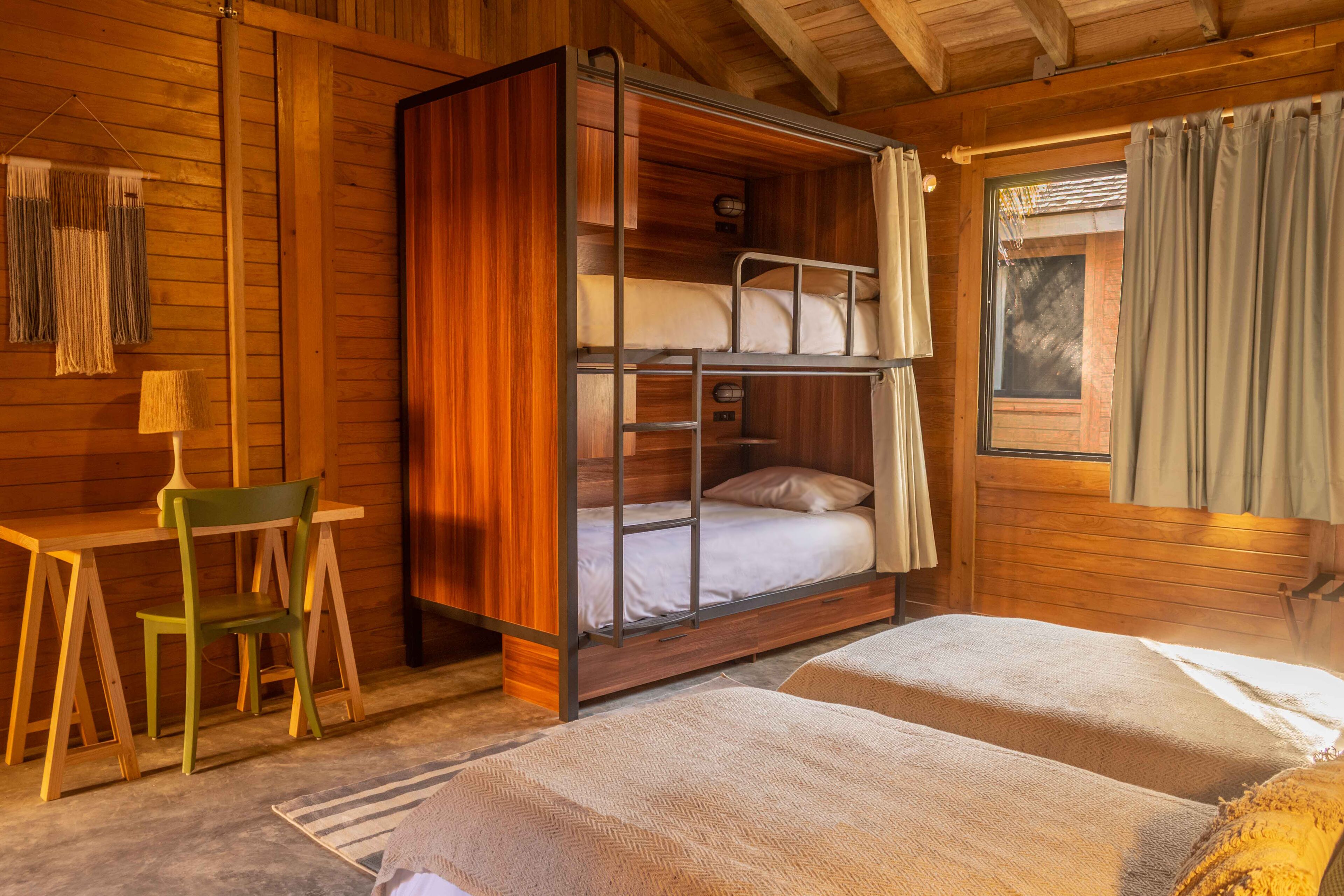 Une chambre dans un chalet en bois, avec des lits superposés, un bureau et une chaise.