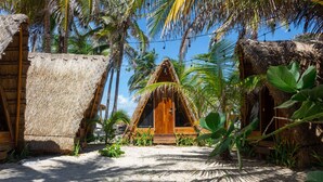 A thatched-roof hut with a wooden door, surrounded by palm trees and a sandy ground. - Nílu Isla Mujeres by Selina (Isla Mujeres)