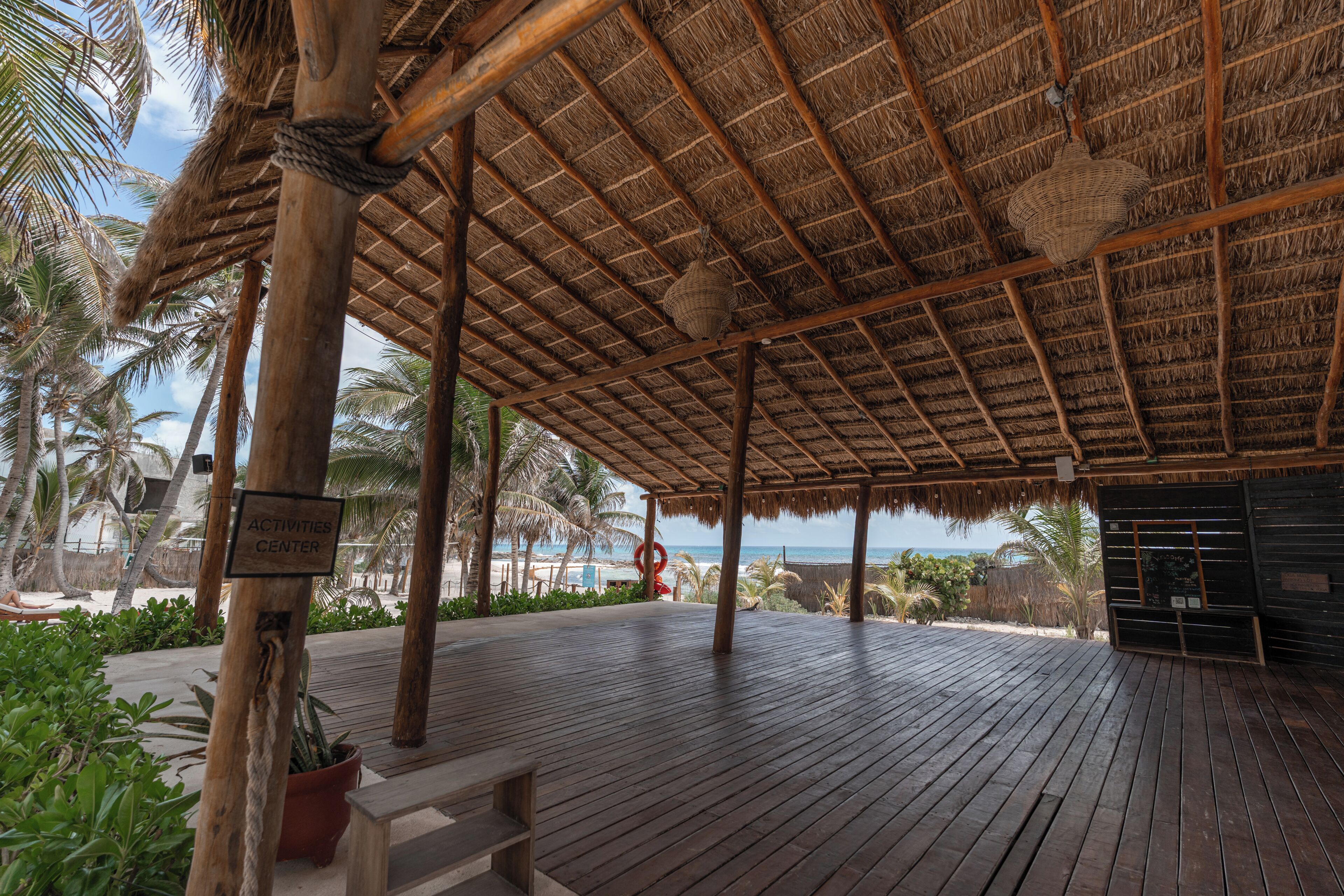 A covered wooden deck with a thatched roof, palm trees, and a sign indicating an activities center.
