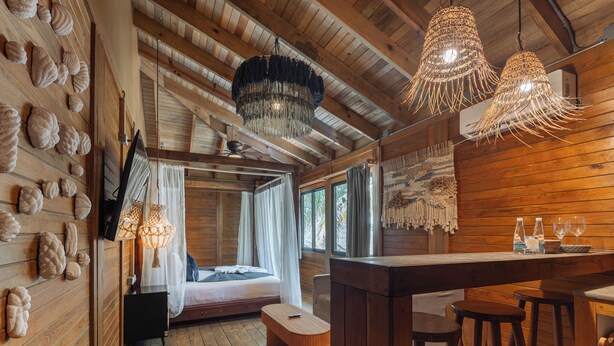 A wooden cabin interior with a bed, a bar area, and a ceiling fan. - Nílu Isla Mujeres by Selina (Isla Mujeres)