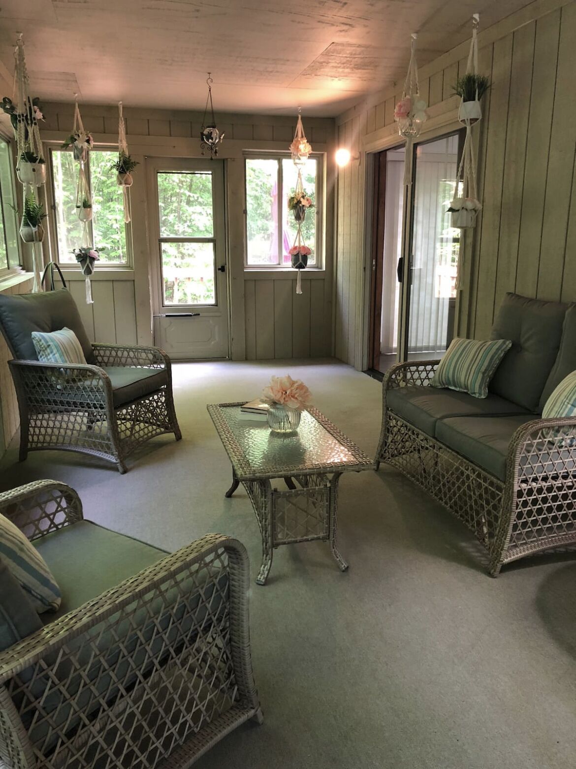 A cozy room with wicker furniture, a glass coffee table, and hanging plants.