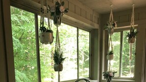 A cozy room with a green sofa, a hanging plant swing, and large windows with a view of greenery. - Escape to ‘Pursue Happiness’ - Your Poconos Retreat! (Tobyhanna)