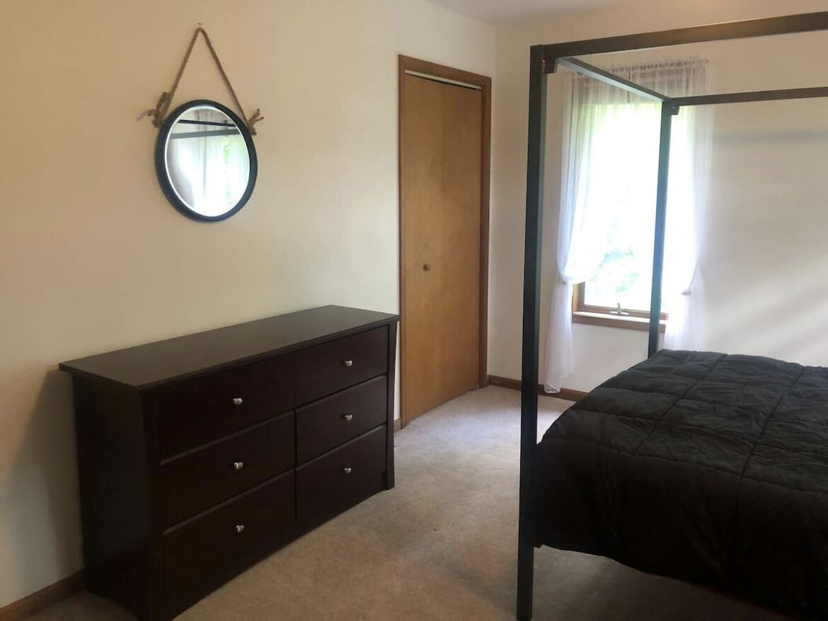 A bedroom with a bed, a dresser, a door, and a window with curtains.