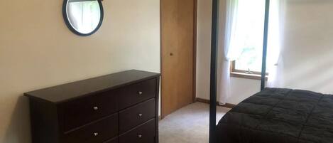 A bedroom with a bed, a dresser, a door, and a window with curtains.