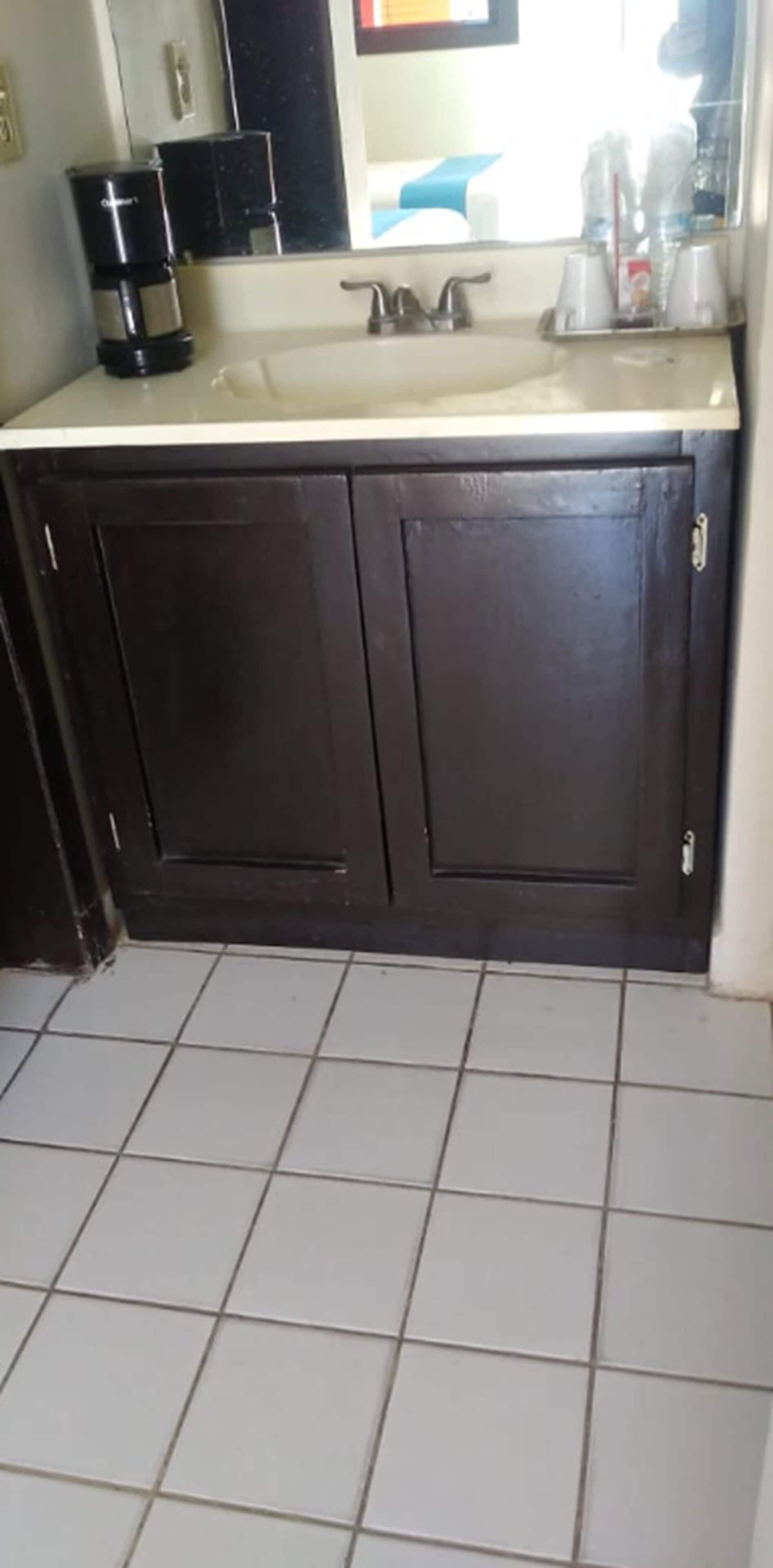 A bathroom with a dark wooden cabinet, a white sink, and a coffee maker.