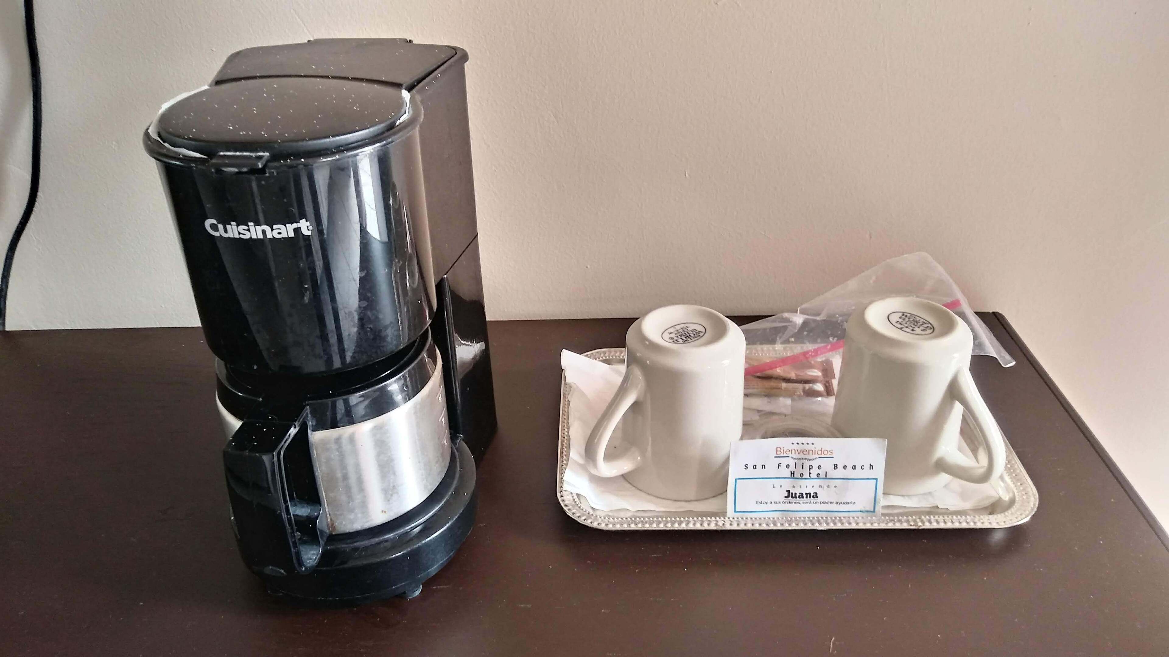 A Cuisinart coffee maker on a table with a tray containing two white cups and a small bag of coffee pods.