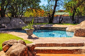 Une piscine bordée de pierres, entourée de rochers et de verdure.