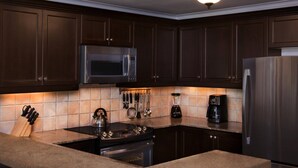 A kitchen with dark wooden cabinets, a stainless steel refrigerator, a microwave, a stove, and a coffee maker.