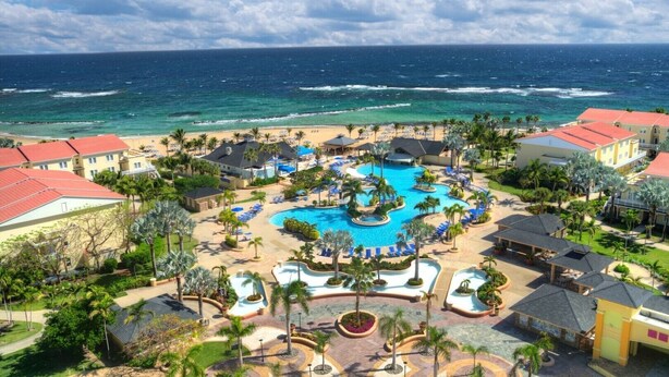 A resort with a central pool, beachfront villas, and a view of the ocean.