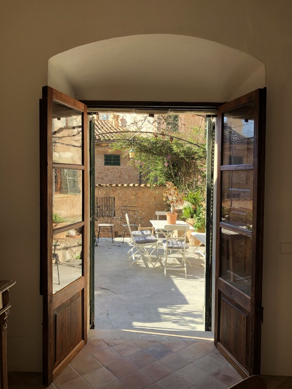 An open doorway leading to an outdoor patio with a table and chairs, a potted plant, and a stone wall.