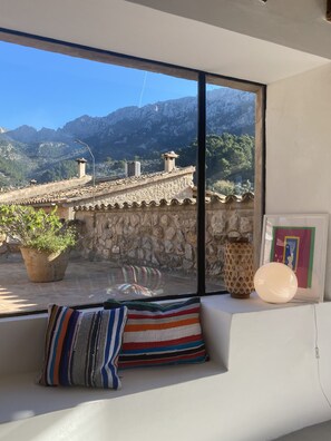 A room with a large window overlooking a mountainous landscape, a stone wall, a potted plant, a striped pillow, and a framed picture.