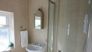 Baño con inodoro, lavamanos y ducha con mampara de vidrio.