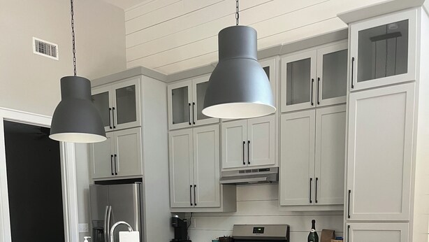 Een moderne keuken met witte kasten, een groot eiland met barstoelen, roestvrijstalen apparatuur en hanglampen.