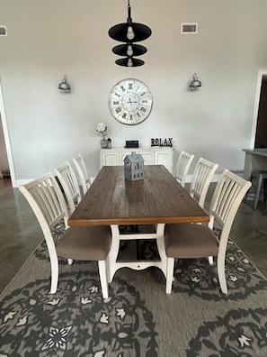 A dining room with a wooden table, white chairs, a wall clock, and a 'RELAX' sign.