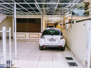 Une voiture blanche est garée dans un parking couvert, dont le sol est carrelé et le toit est constitué d’une structure métallique.